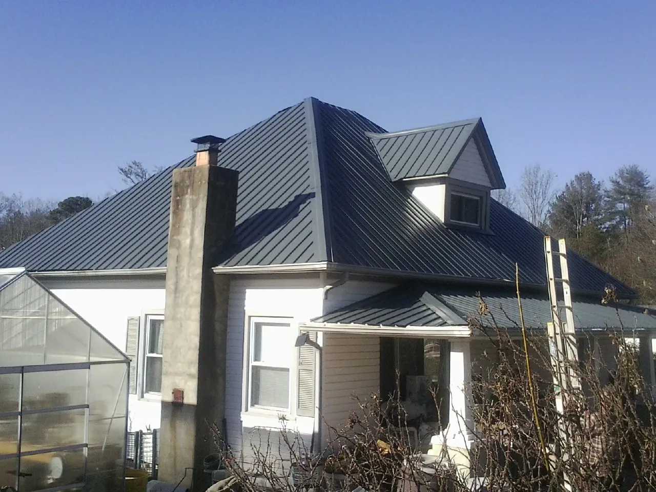 Dark blue standing seam metal roof on a white farmhouse with dormer — Slate & Tile Roof Repair by Roofing Brothers in Lakeshore
