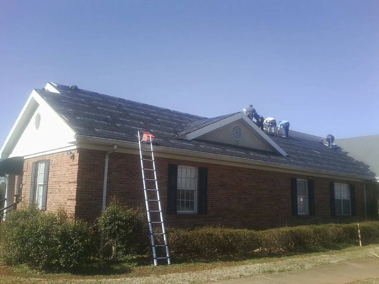 Crew tearing shingles off a brick ranch roof with a ladder set — Metal Roof Repair work by our crew in Lakeshore