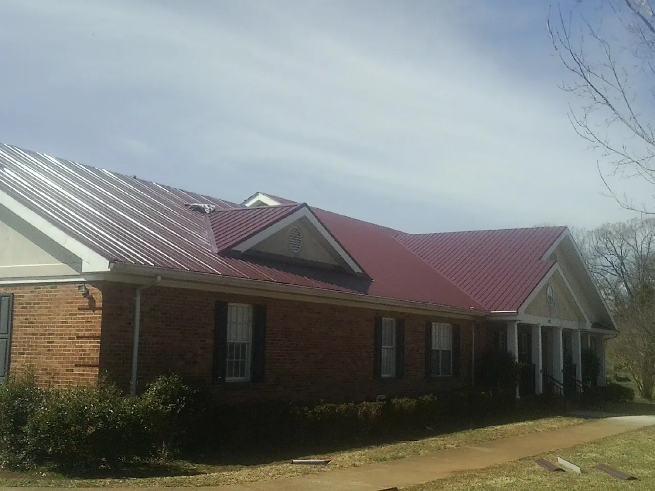 Red metal roof with gabled entries on a long brick building, from a Hail Damage Roof Repair job in Lakeshore