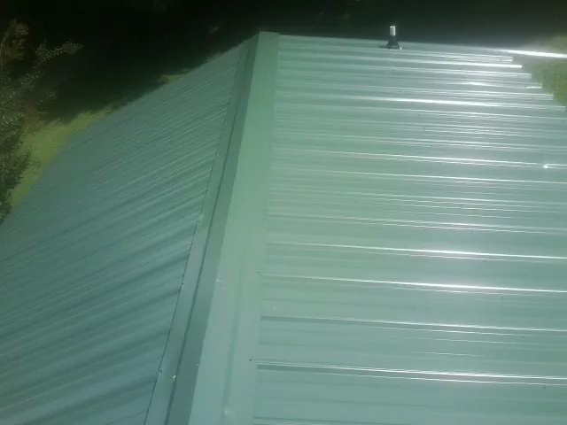 New green metal panels meeting at the ridge of a roof — Flat Roof Repair work by our crew in Lakeshore