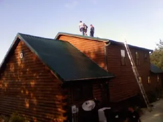 Crew on the ridge of a green metal roof on a two story log home in Lakeshore