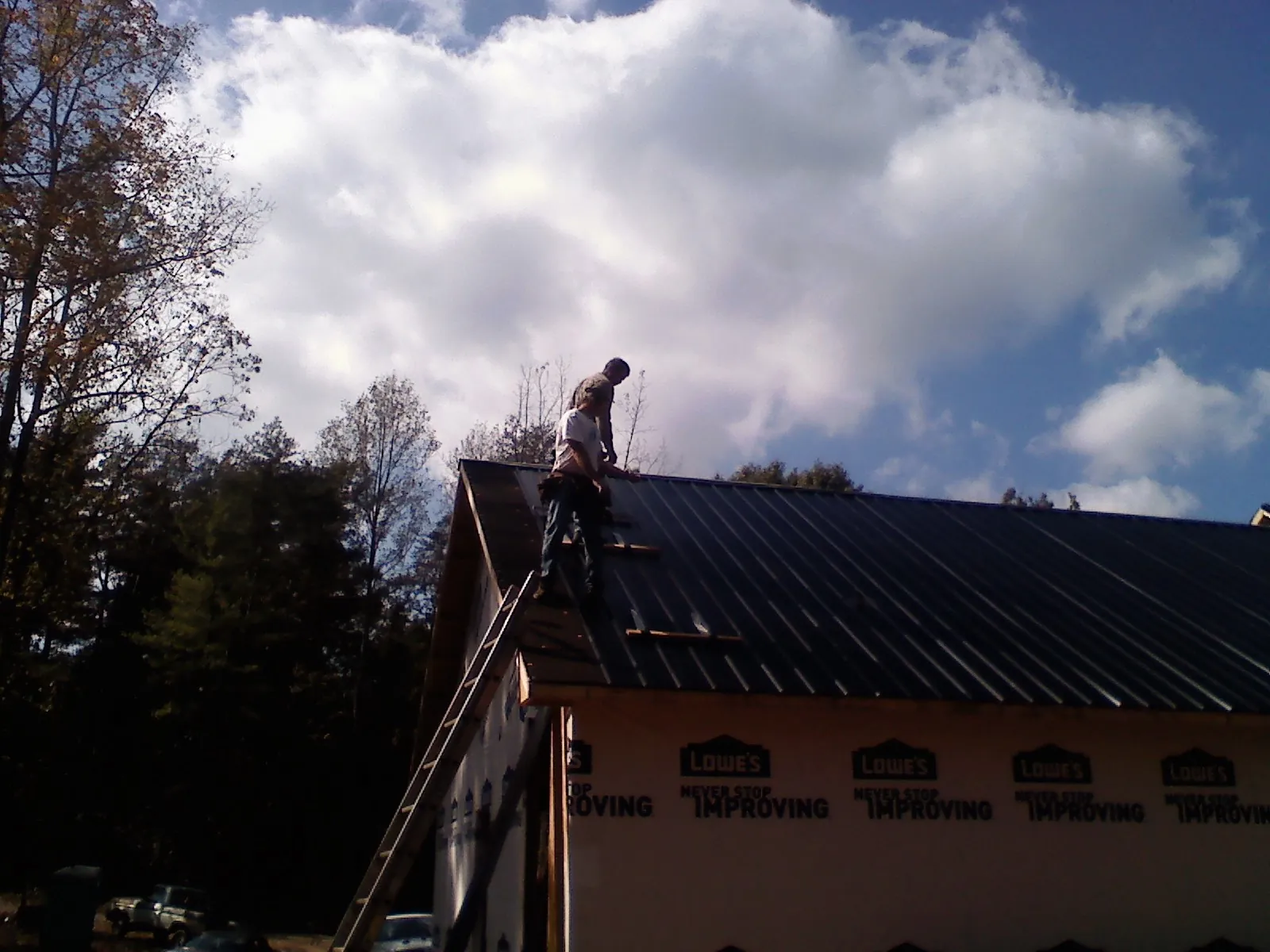 Roofer fastening dark metal panels high against a cloudy sky, from a Roof Inspection job in Lakeshore